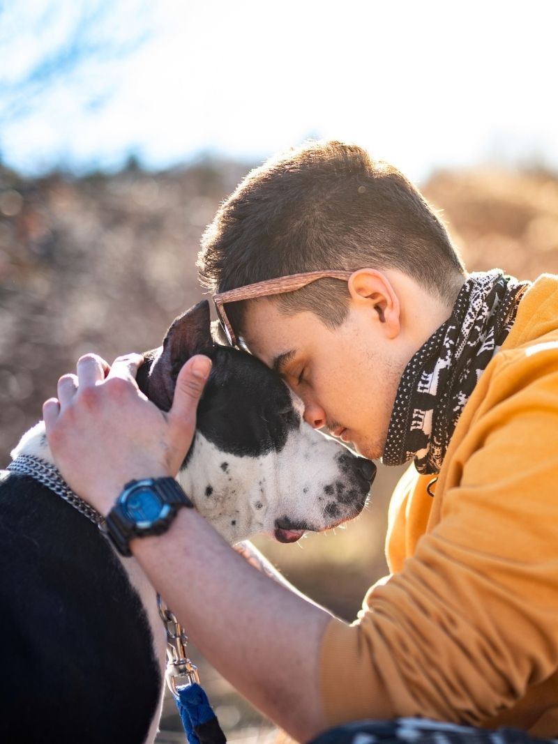 young man softly embracing his dog outdoors