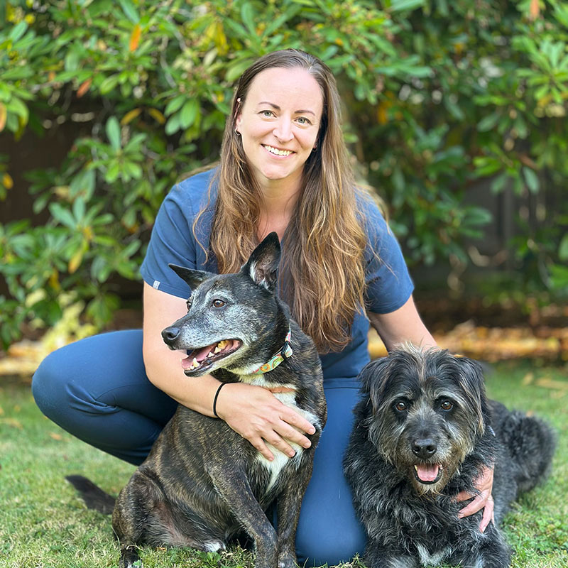 portrait of Dr. Clare Peterson smiling with her dogs outside